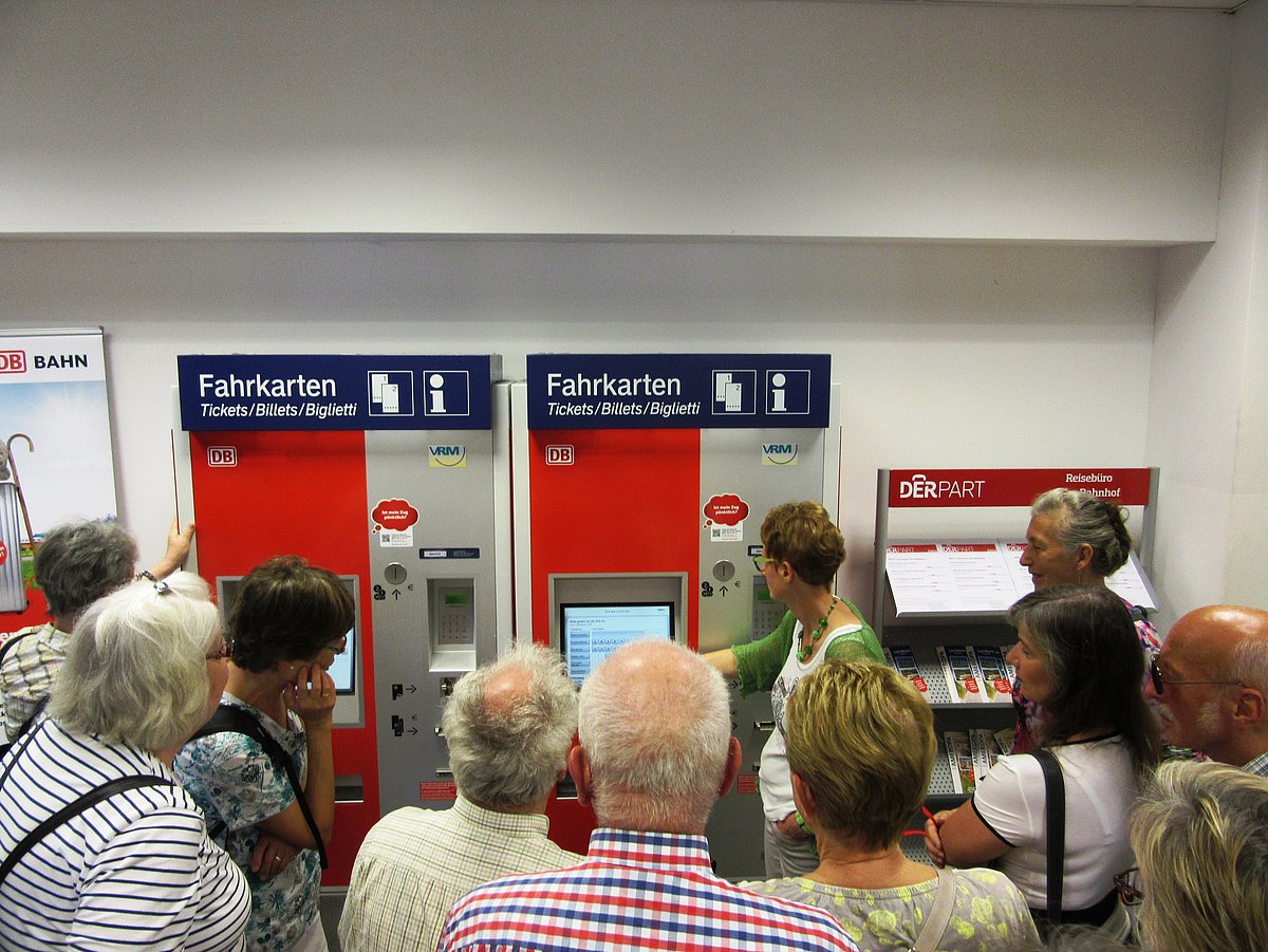 Personengruppe steht vor Fahrkartenautomat in einem Bahnhof