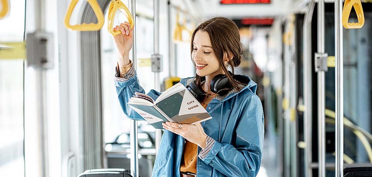 Junge Frau steht im Bus und liest ein Buch