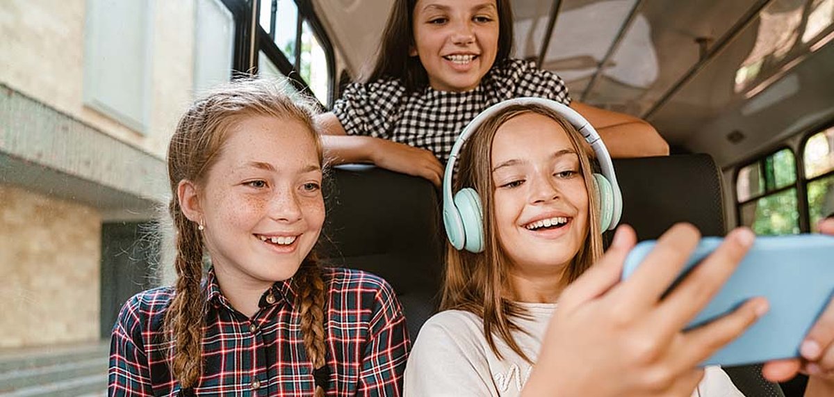 [Translate to English:] Drei Schüler schauen sich im Bus etwas auf dem Tablet an