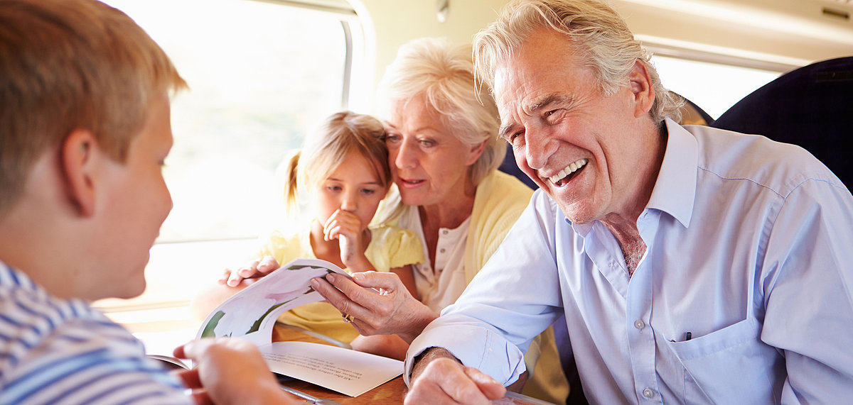 Älteres Ehepaar mit Enkelkindern sitzen im Zug an einem Tisch