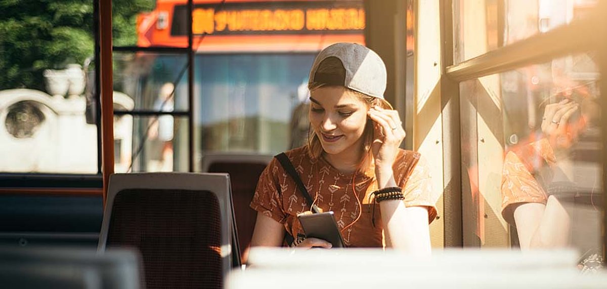 [Translate to English:] Junge Frau sitzt im Bus und hört Musik