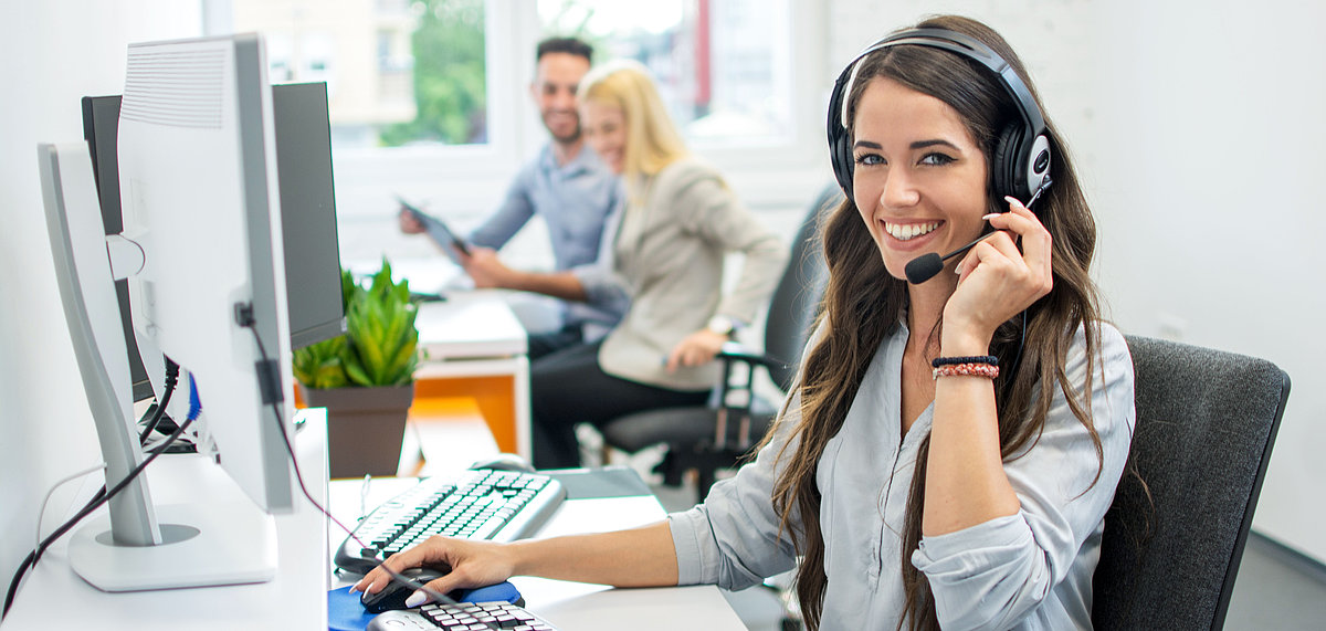 [Translate to English:] Frau mit Headset sitzt vor einem Computer